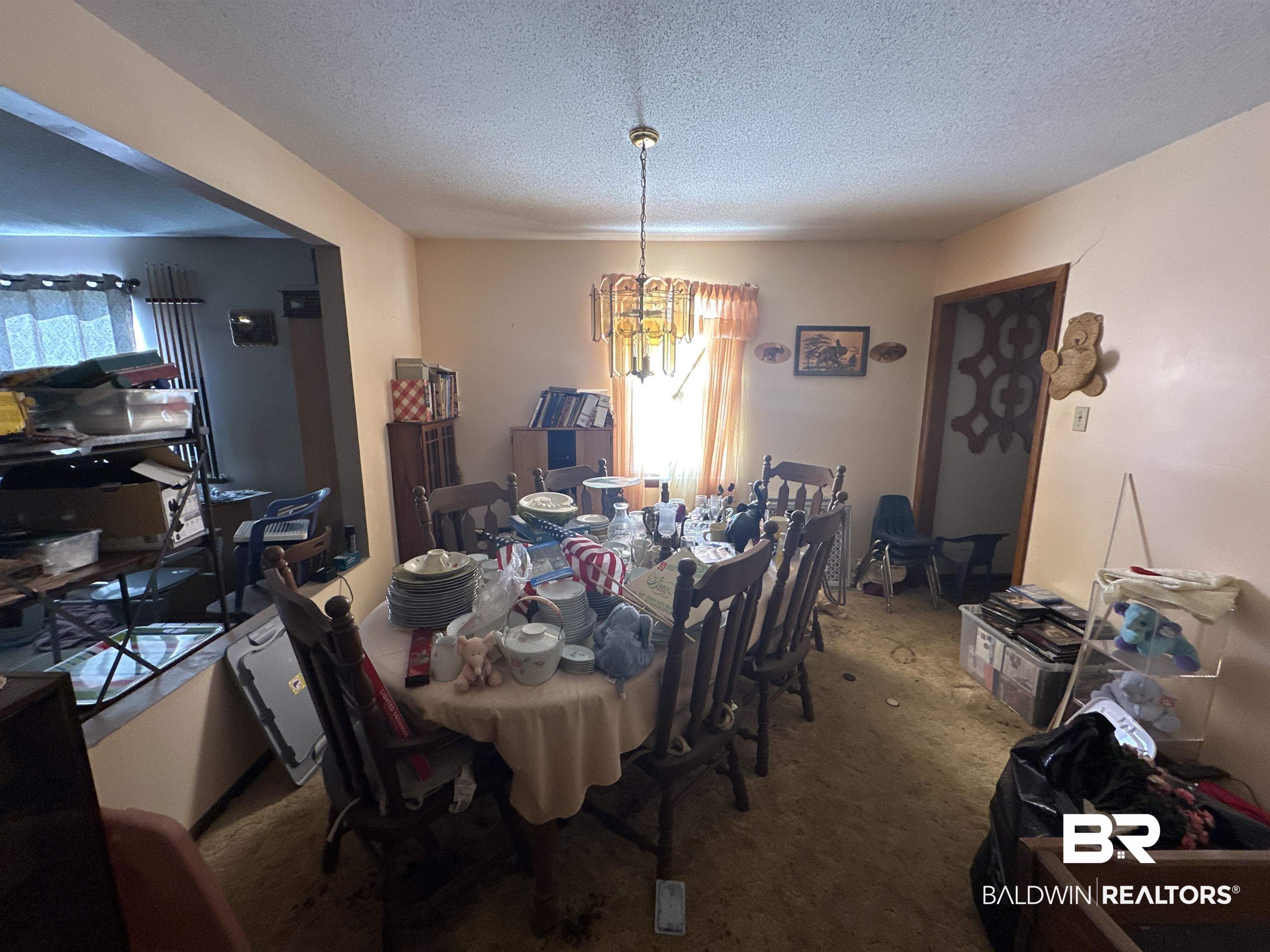 9520 C Four Mile Road Irvington, AL 36544 - Photo 10 of 32 Carpeted dining room featuring a chandelier, a textured ceiling, and a healthy amount of sunlight