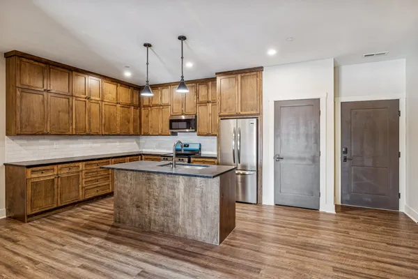 a kitchen with stainless steel appliances granite countertop a refrigerator a sink a stove and a wooden floors