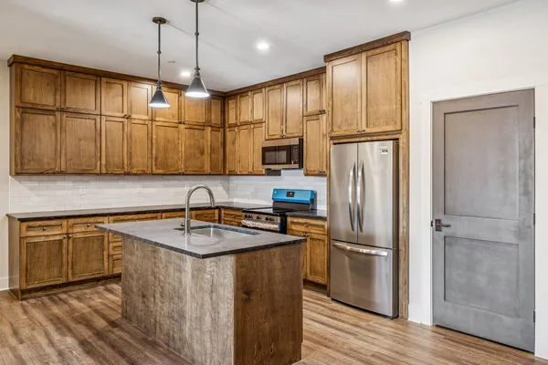 a kitchen with stainless steel appliances granite countertop a refrigerator a sink dishwasher a oven with wooden cabinets and chairs