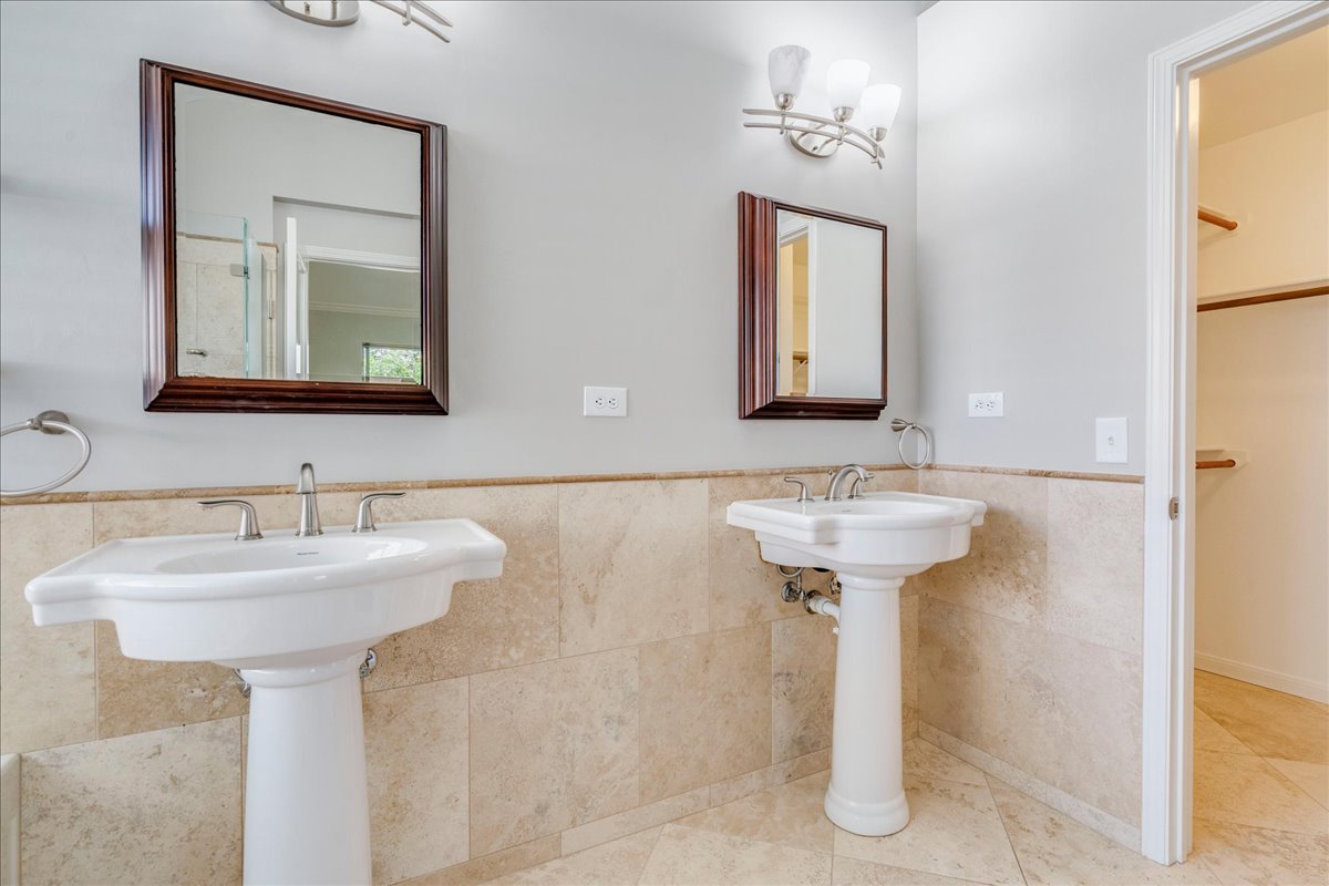 6530 Needham Lane Austin, TX 78739 - Photo 16 of 29 Dual pedestal sinks and neutral stone tile adorn this spacious bathroom, featuring ample natural light and clean lines.