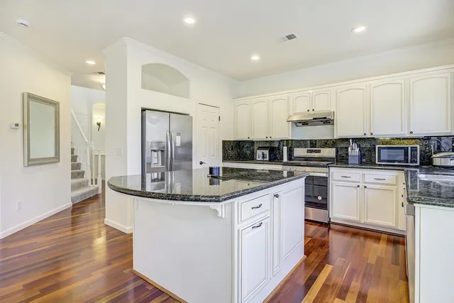 a kitchen with stainless steel appliances granite countertop a stove top oven a sink and white cabinets