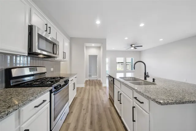 a kitchen with stainless steel appliances granite countertop a sink a stove and a wooden floors