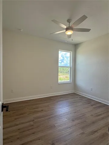 an empty room with wooden floor fan and windows