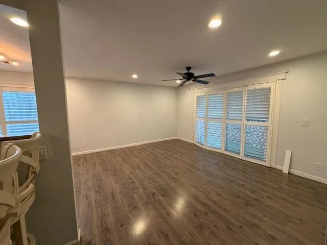 an empty room with wooden floor ceiling fan and windows