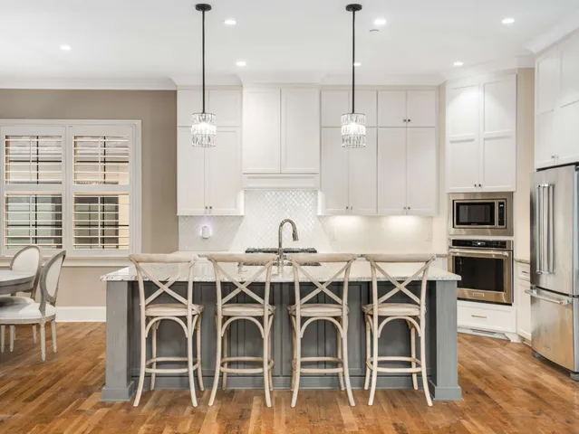 a kitchen with stainless steel appliances a stove a sink a refrigerator a center island a stove and white cabinets with wooden floor