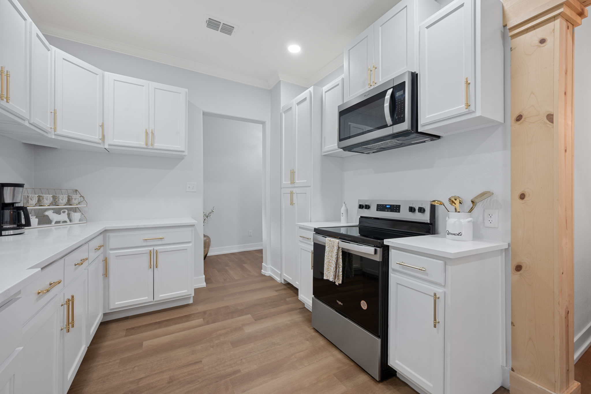 602 East 6th Street Cameron, TX 76520 - Photo 20 of 40 Modern kitchen featuring white cabinetry with gold-tone hardware, wood-finish flooring, stainless steel appliances, and light-toned countertops