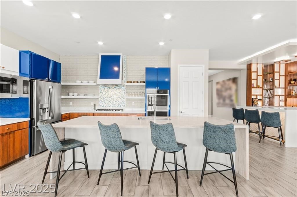 103 Reflection Cove Drive Henderson, NV 89011 - Photo 19 of 66 Kitchen featuring a kitchen breakfast bar, backsplash, light wood-style floors, appliances with stainless steel finishes, and recessed lighting