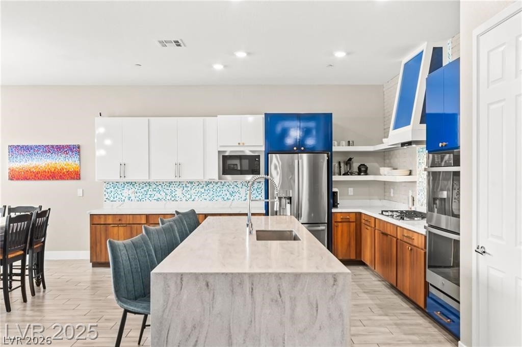 103 Reflection Cove Drive Henderson, NV 89011 - Photo 20 of 66 Kitchen featuring tasteful backsplash, light stone counters, open shelves, an island with sink, and recessed lighting