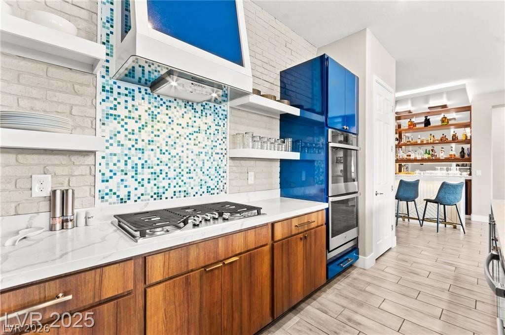 103 Reflection Cove Drive Henderson, NV 89011 - Photo 24 of 66 Kitchen featuring open shelves, light stone counters, wood tiled floors, and backsplash