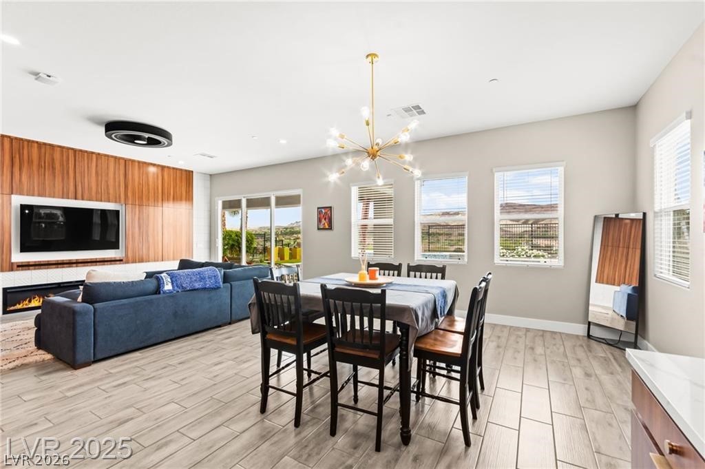 103 Reflection Cove Drive Henderson, NV 89011 - Photo 26 of 66 Dining space featuring wood tiled floors, plenty of natural light, a chandelier, and a lit fireplace