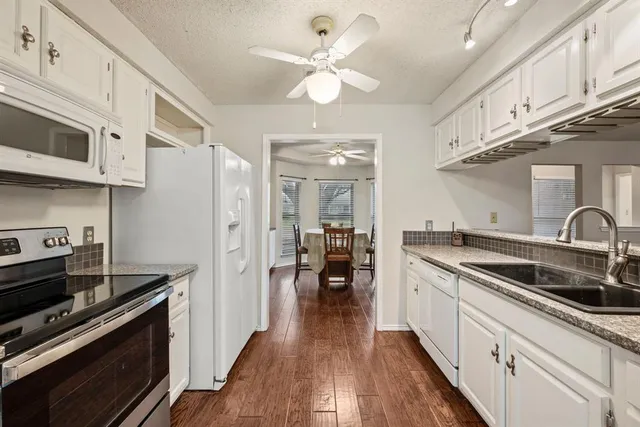 a kitchen with stainless steel appliances a sink dishwasher stove and white cabinets with wooden floor