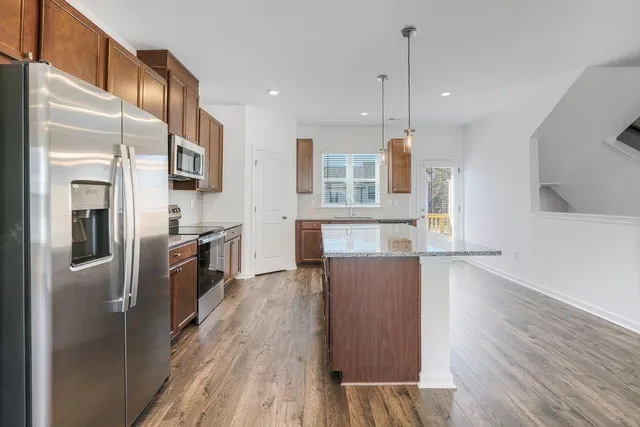 a kitchen with stainless steel appliances granite countertop a refrigerator a stove oven a sink dishwasher and a refrigerator with wooden floor