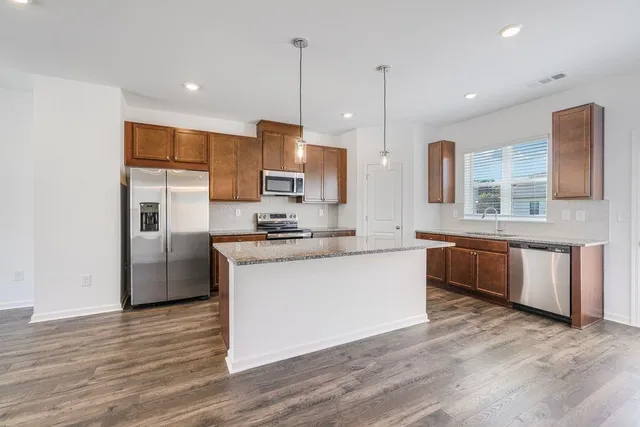 a large kitchen with stainless steel appliances kitchen island granite countertop a stove a sink a refrigerator and a wooden floor