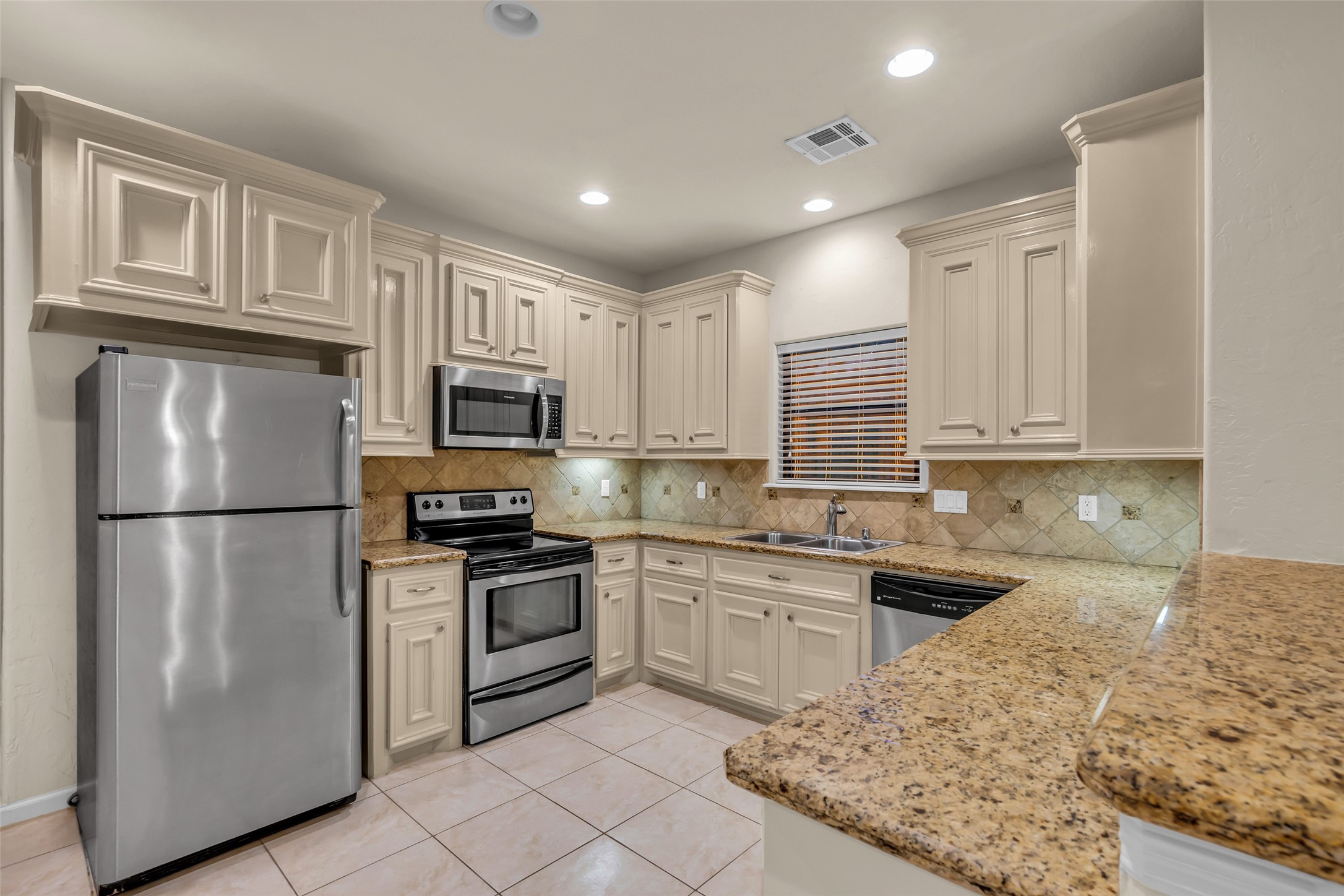 1898 Longmire Road, Unit 5 Conroe, TX 77304 - Photo 19 of 48 This kitchen features stainless steel appliances, ample cream-colored cabinetry, and granite countertops. It has a tiled backsplash, recessed lighting, and a window above the sink for natural light.