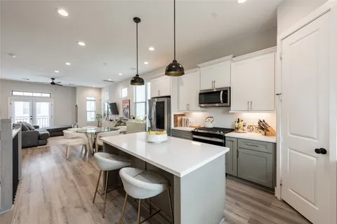 a kitchen with stainless steel appliances a stove a sink a microwave a refrigerator white cabinets and wooden floor