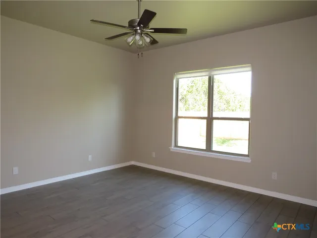 an empty room with wooden floor fan and windows