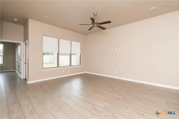 an empty room with wooden floor fan and windows