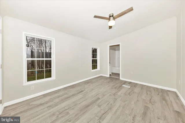 an empty room with wooden floor ceiling fan and windows
