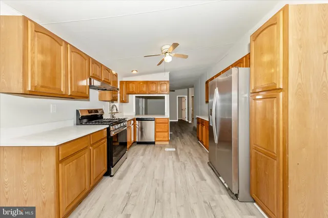 a kitchen with stainless steel appliances a refrigerator a sink dishwasher a stove and white cabinets with wooden floor