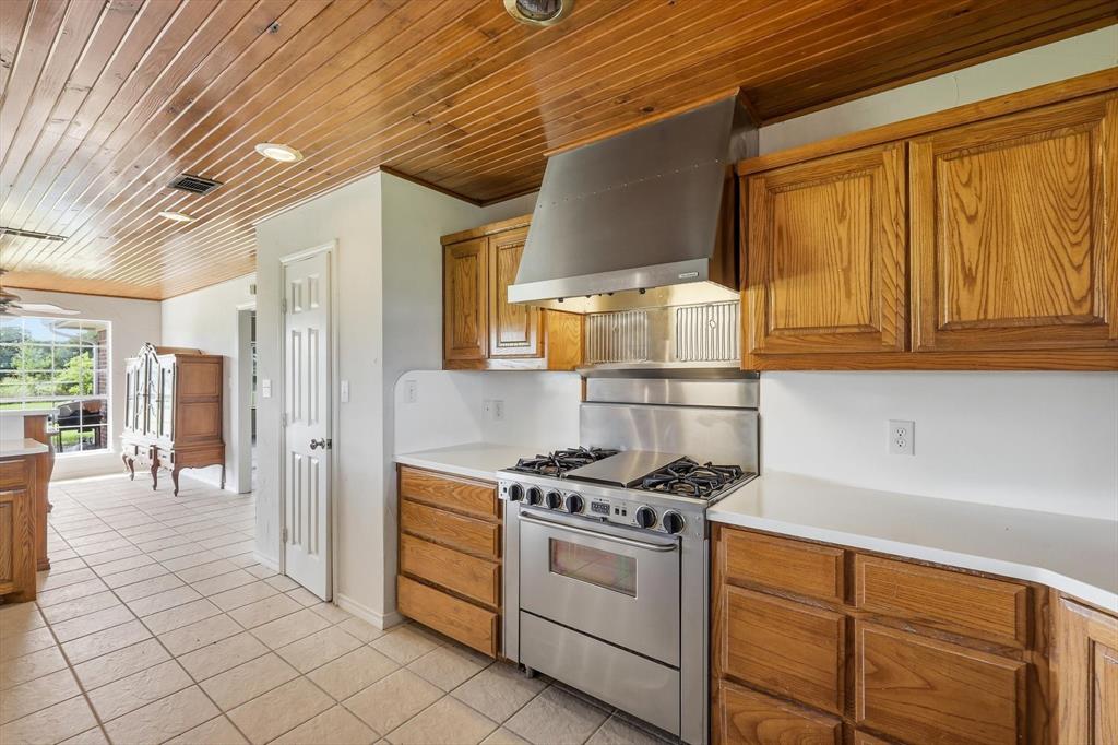 12190 Bell Road Pilot Point, TX 76258 - Photo 16 of 39 Kitchen featuring a stainless steel professional-grade range with a matching vent hood, wood-finish cabinetry, light-toned countertops, and tile flooring