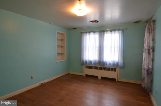 an view of an empty room with wooden floor and a window