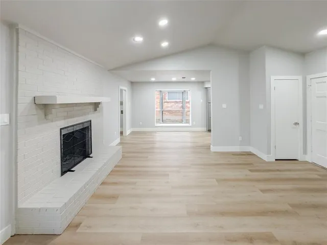 a view of an empty room with wooden floor fireplace and a window