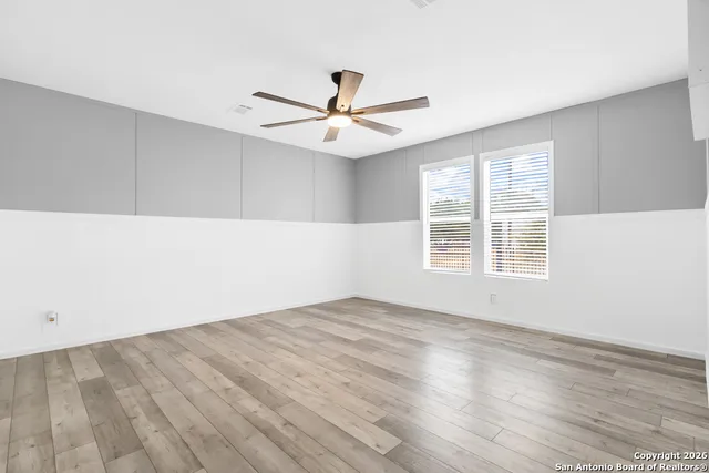 an empty room with wooden floor ceiling fan and windows