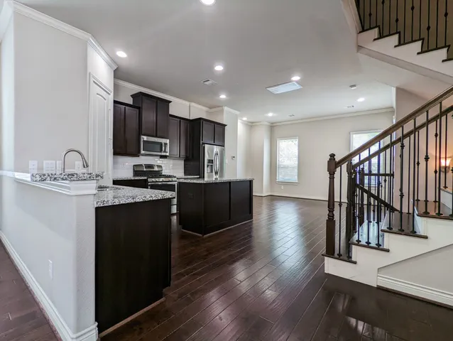 a kitchen with stainless steel appliances granite countertop a refrigerator a sink dishwasher a stove and a microwave oven on the wooden floor