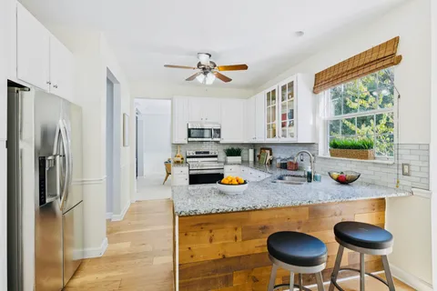 a kitchen with stainless steel appliances granite countertop a refrigerator a stove a sink a dining table and chairs with wooden floor