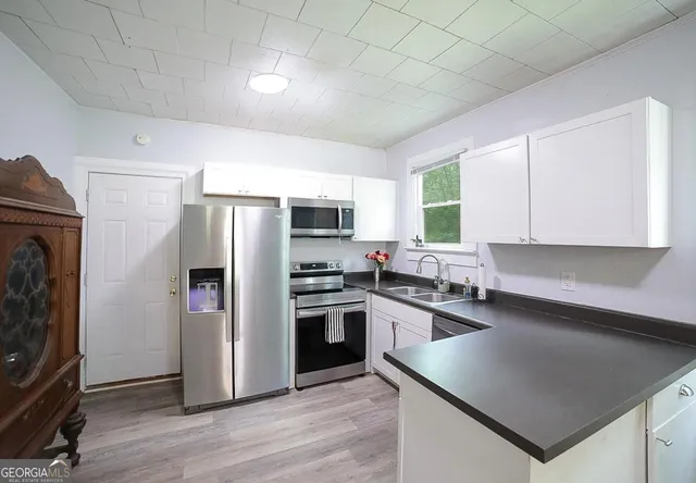 a kitchen with stainless steel appliances granite countertop a refrigerator a sink dishwasher a stove top oven a refrigerator and white cabinets with wooden floor