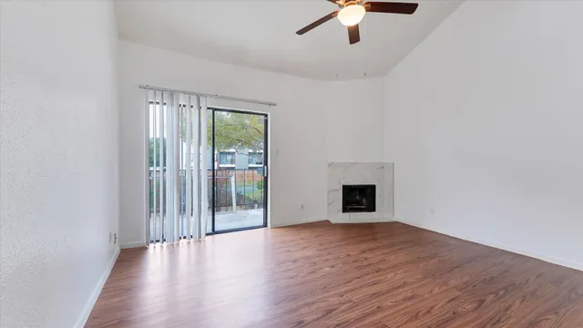 an empty room with wooden floor chandelier fan and windows