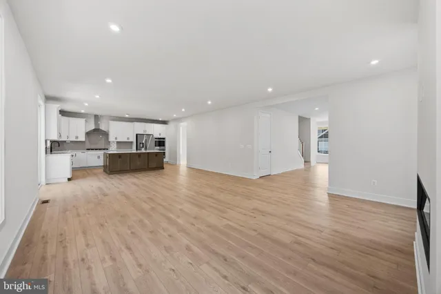 a view of empty room with wooden floor and kitchen