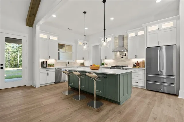 a kitchen with stainless steel appliances a stove a sink dishwasher a refrigerator and white cabinets with wooden floor