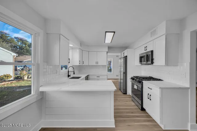 a large white kitchen with granite countertop a large counter top stainless steel appliances and a window