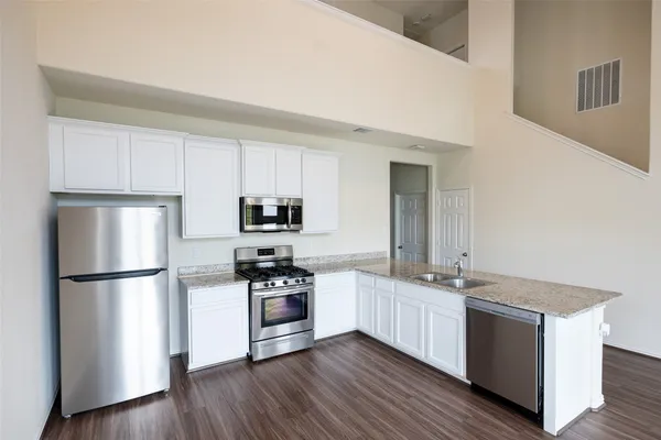 a kitchen with stainless steel appliances granite countertop a refrigerator a stove a sink and white cabinets with wooden floor
