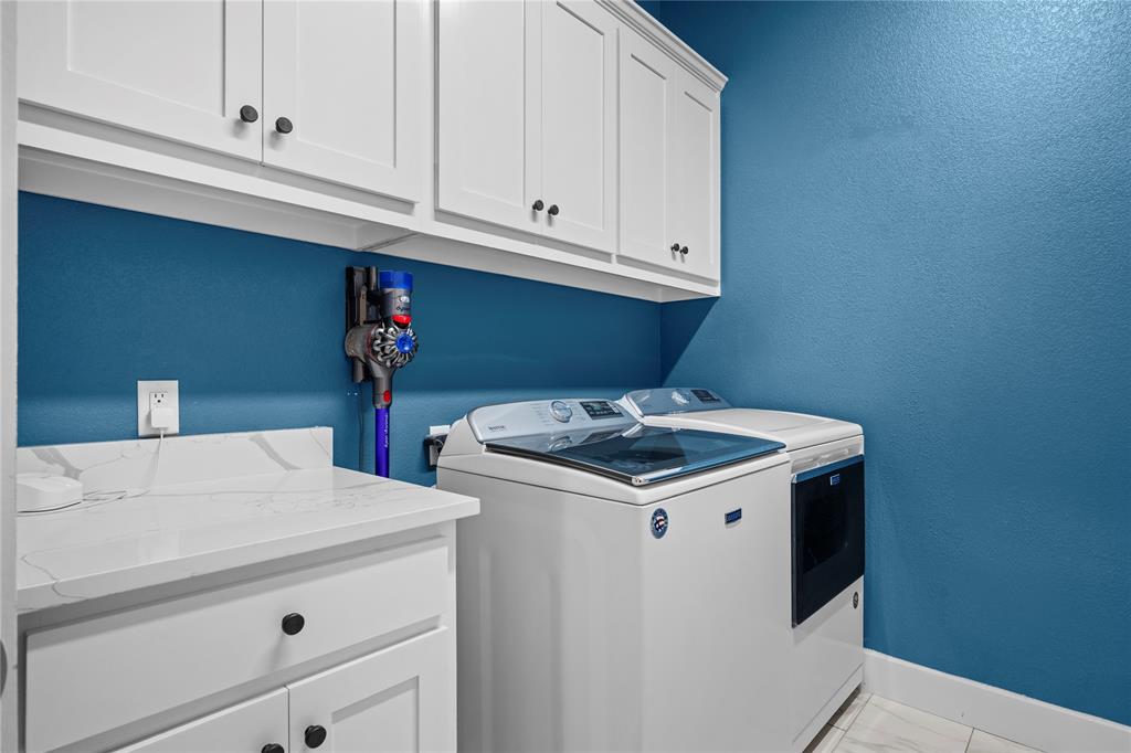 1024 Henry Way Springtown, TX 76082 - Photo 24 of 29 Laundry area featuring white cabinetry with black hardware, a light-colored countertop with veining, and a vibrant blue wall color