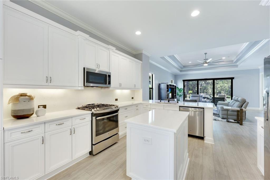 Kitchen with peninsula, white quartz counters, stainless appliances, light wood-type flooring, decorative light fixtures, and white cabinets