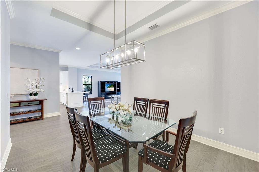 6592 Roma Way Naples, FL 34113 - Photo 12 of 41 Dining space with a tray ceiling, crown molding, light wood-style flooring, and an inviting chandelier