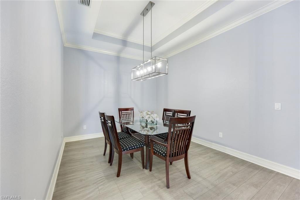 6592 Roma Way Naples, FL 34113 - Photo 13 of 41 Dining space with a tray ceiling, crown molding, light wood-style flooring, and an inviting chandelier