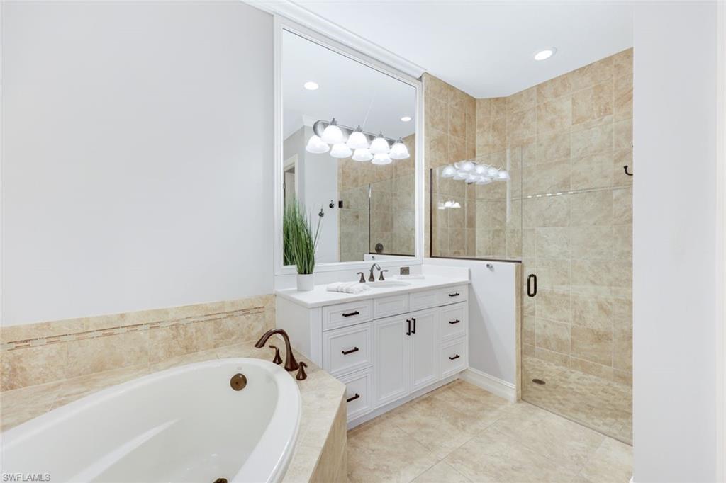 6592 Roma Way Naples, FL 34113 - Photo 18 of 41 Primary bathroom with tile patterned floors, white cabinetry, quartz counters, soaking tub and frameless shower door