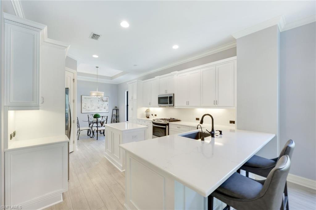 Kitchen with peninsula, white quartz counters, stainless appliances, light wood-type flooring, decorative light fixtures, and white cabinets