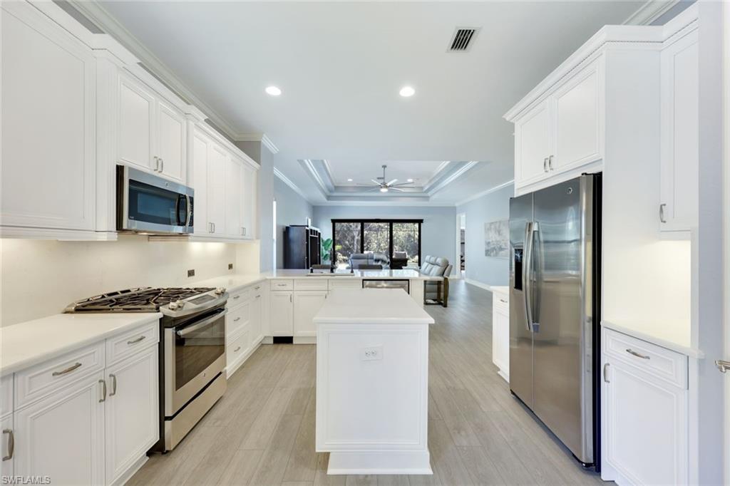 Kitchen with peninsula, white quartz counters, stainless appliances, light wood-type flooring, decorative light fixtures, and white cabinets