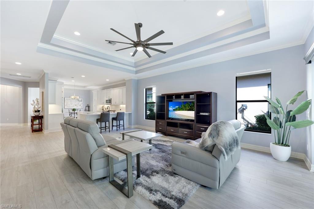 6592 Roma Way Naples, FL 34113 - Photo 9 of 41 Living room featuring a tray ceiling, crown molding, ceiling fan, and light wood-style floors