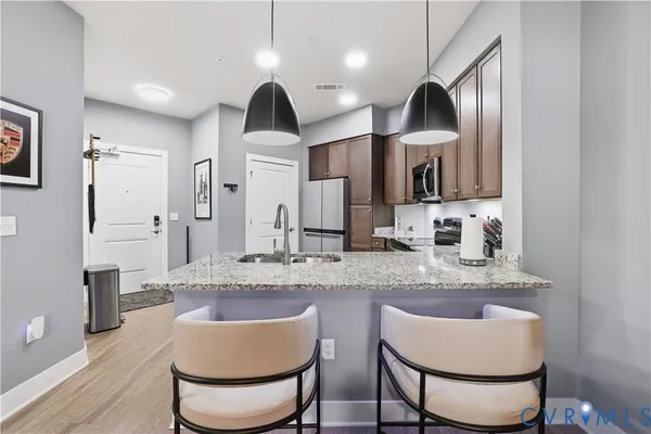 a kitchen with stainless steel appliances granite countertop a sink a stove a refrigerator and a dining table with wooden floor