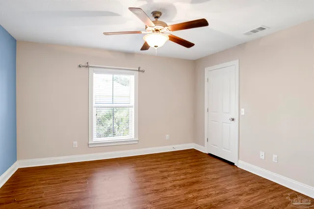 an empty room with wooden floor ceiling fan and windows