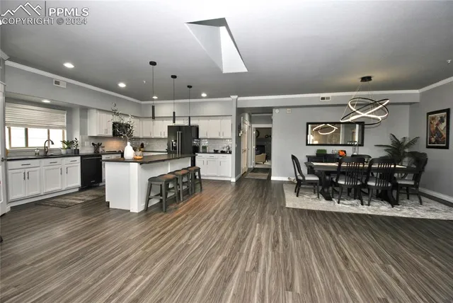 a kitchen with stainless steel appliances a refrigerator a stove top oven a dining table and chairs with wooden floor