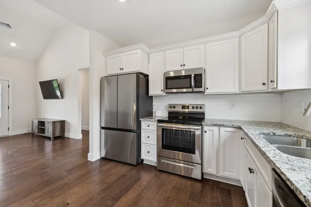 a kitchen with granite countertop a refrigerator a stove a sink and white cabinets