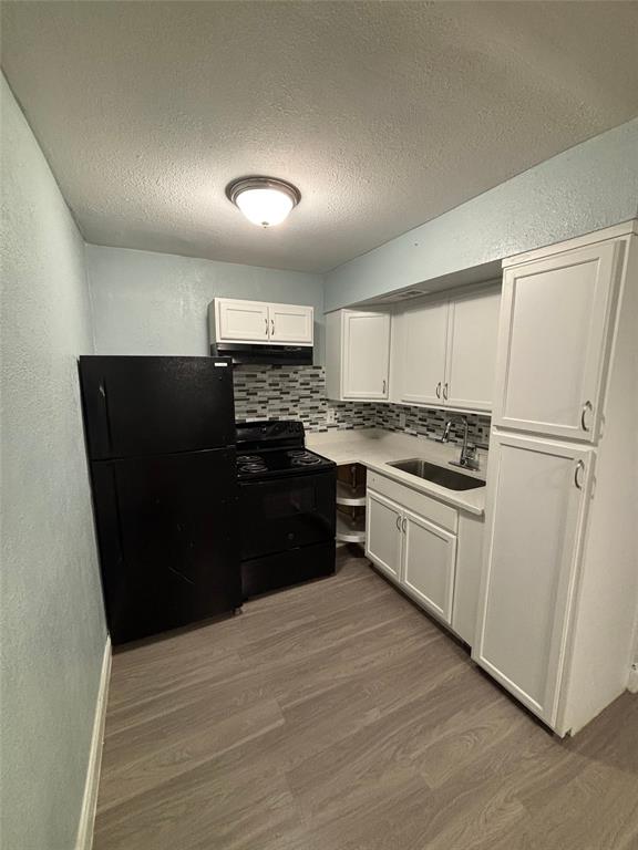 301 Rolston Road, Unit 315101 Irving, TX 75060 - Photo 11 of 12 Kitchen featuring white cabinetry, mosaic tile backsplash, black appliances, a single basin sink, and wood-finish flooring