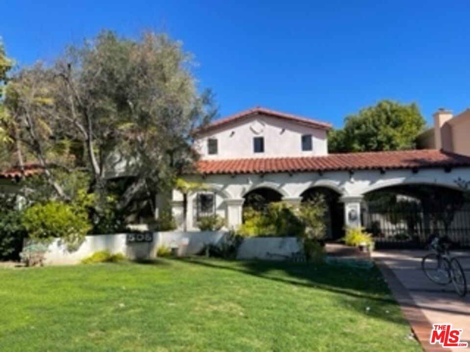 a view of a white house with large trees and plants