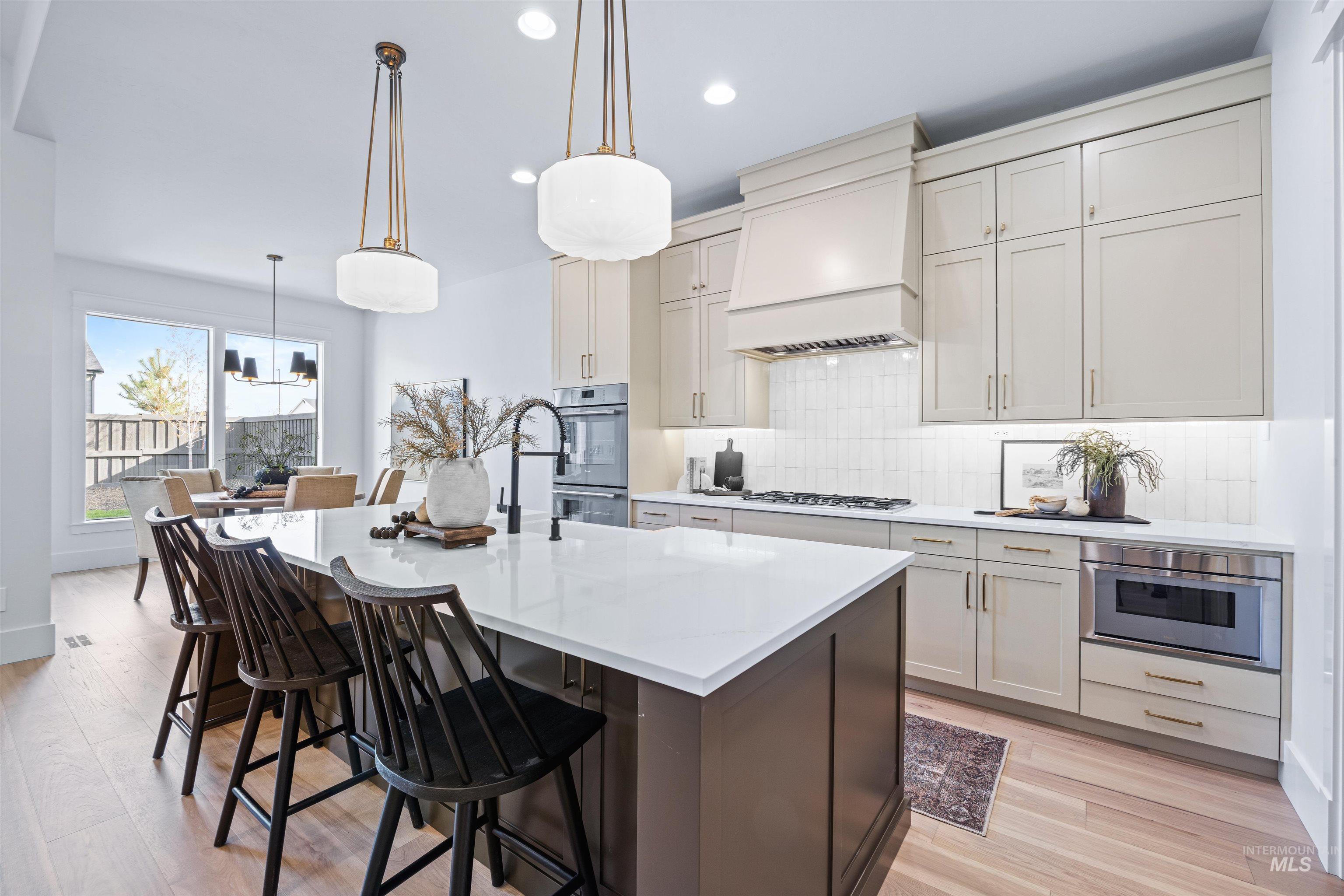948 East Escalation Street Meridian, ID 83642 - Photo 16 of 44 Two tone kitchen with dual tone cabinets, an island with sink, light stone countertops, a breakfast bar, and decorative backsplash
